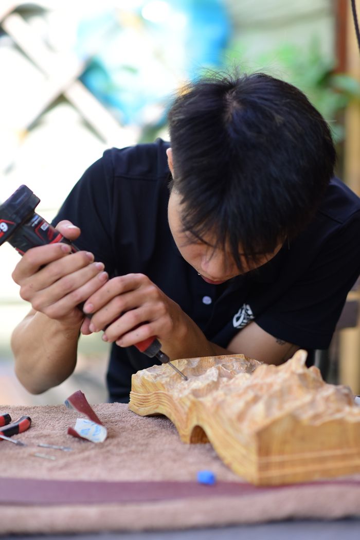Focused craftsman carving detailed wooden sculpture using a drill outdoors.